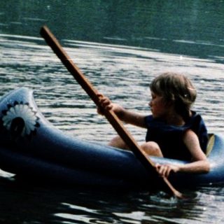 Children paddling inflatable boats on calm lake.