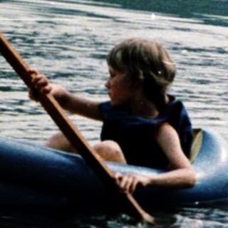 Children paddling inflatable boats on calm lake.
