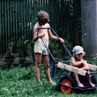Two children pushing a wagon in a backyard.