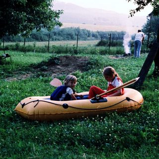Two children playing in an inflatable boat on grass.