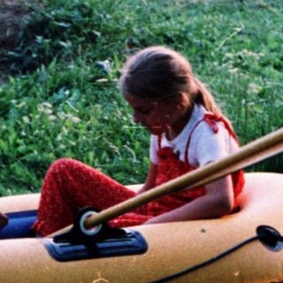 Two children playing in an inflatable boat on grass.