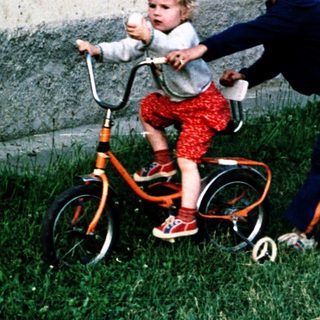 Young child learning to ride a bike with adult assistance.