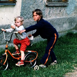 Young child learning to ride a bike with adult assistance.