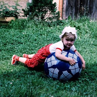 Child playing with large exercise ball outdoors.