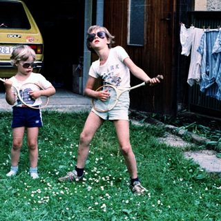 Two children playing with tennis rackets outdoors.