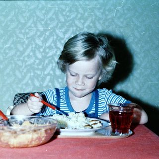 Child eating cake with fork at table.