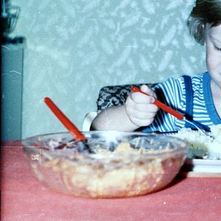 Child eating cake with fork at table.