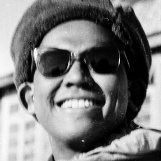 Young person smiling outdoors wearing sunglasses, beret, and backpack.