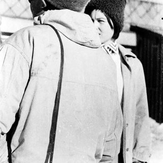 Two people wearing winter clothing standing closely outdoors.
