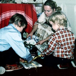 Family opening Christmas presents by decorated tree.