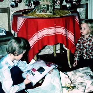 Two children opening wrapped gifts indoors.