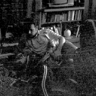 Man in chaotic room holding laptop, surrounded by debris.