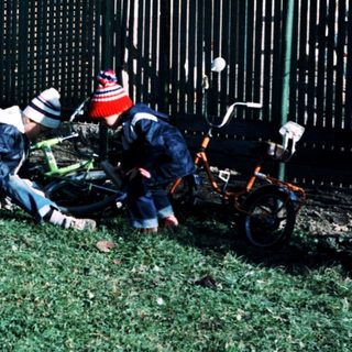 Two children playing with a fallen bicycle in yard.