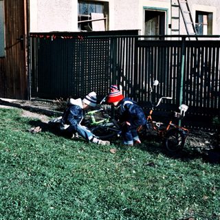 Two children playing with a fallen bicycle in yard.