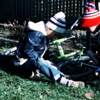 Two children playing with a fallen bicycle in yard.