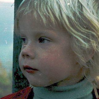 Young child gazing thoughtfully through wooden fence.