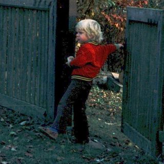 Child playing outside near wooden fence.
