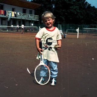 Young boy holding tennis racket on court.