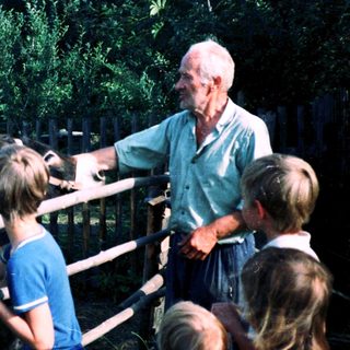 Old man feeding animals with children observing.