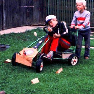 Two people mowing grass with a child in a cart.