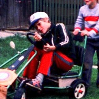 Two people mowing grass with a child in a cart.