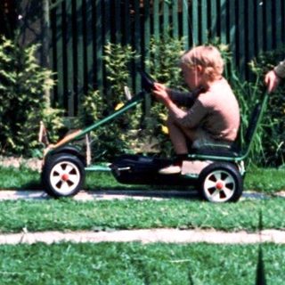 Child riding lawn mower in backyard.