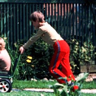 Child riding lawn mower in backyard.