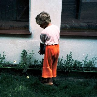 Child bending to pick flower near building.