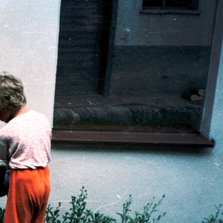 Child bending to pick flower near building.