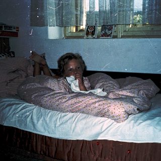 Child lying in bed reading under dim light.