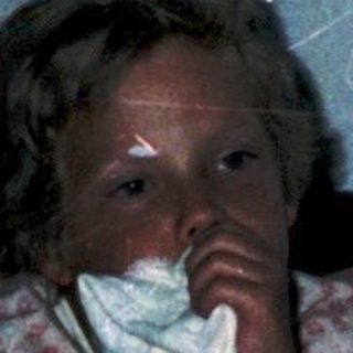 Child lying in bed reading under dim light.