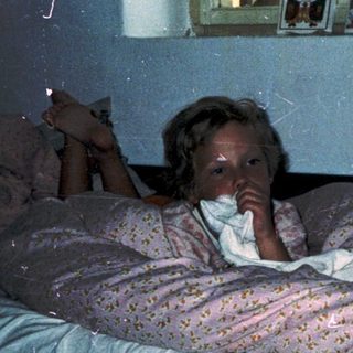 Child lying in bed reading under dim light.