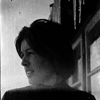Woman smiling outdoors with icicles on building.