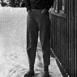 Smiling person standing in snow near fence.