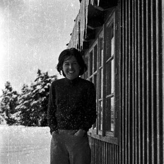 Smiling person standing in snow near fence.