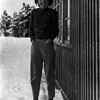 Smiling person standing in snow near fence.
