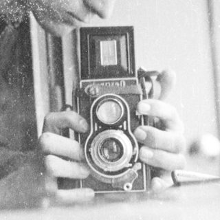 Person using vintage twin-lens reflex camera indoors.