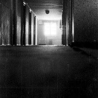 Dark hallway with dimly lit rooms ahead.