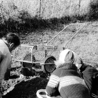Two people operating portable water well drilling equipment.