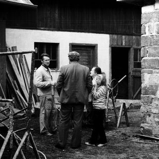 People discussing near a rustic building with construction tools.