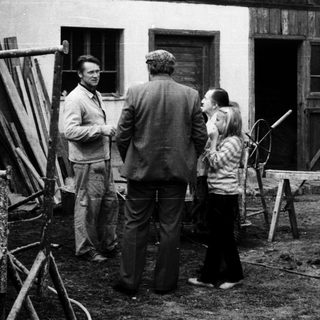 People discussing near a rustic building with construction tools.