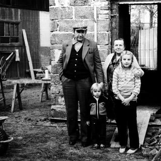 Family posing outside rustic stone house.