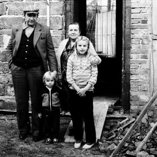 Family posing outside rustic stone house.