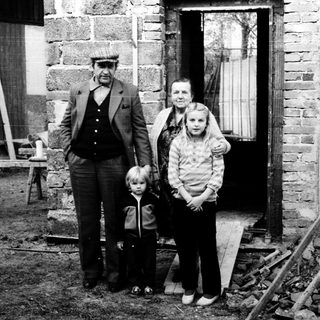 Family posing outside rustic stone house.