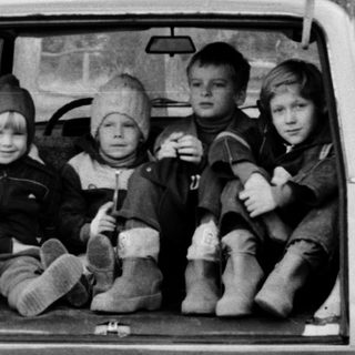 Four children sitting in open car trunk in forest.