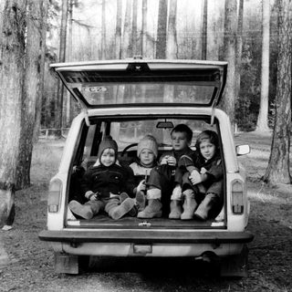Four children sitting in open car trunk in forest.
