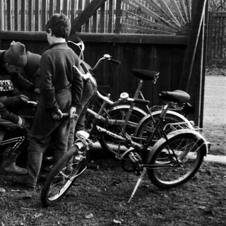 Three teens leaning against fence near parked bicycle.