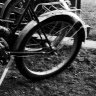 Three teens leaning against fence near parked bicycle.