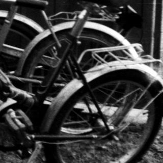 Three teens leaning against fence near parked bicycle.