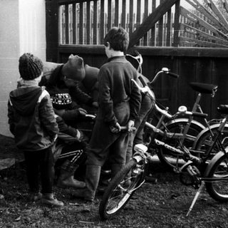 Three teens leaning against fence near parked bicycle.